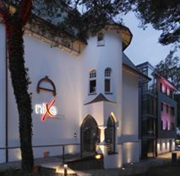 Projekt aus der Entwurf-Galerie von Falk Architekturbüro: weißes Gebäude mit Erker und beleuchteter Fassade in der Abenddämmerung